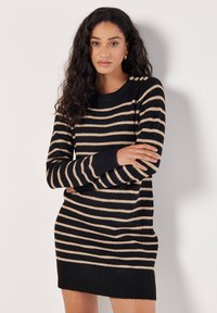 Abito a maglia a righe nero e beige con colletto tondo e tre bottoni decorativi sulla spalla. Texture a coste sui polsini e sull'orlo.