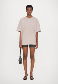Oversized soft pink cotton t-shirt with short sleeves, paired with gray denim shorts, holding a black handbag, and wearing black strappy sandals.