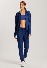 Conjunto atlético de color azul marino que incluye una chaqueta con cremallera, un top corto y pantalones con cordón en un material suave. Zapatillas blancas completan el atuendo.