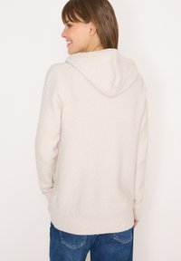 Sweat à capuche beige clair en matériau doux et texturé, avec des poignets et un ourlet côtelés, offrant une coupe décontractée et présenté vu de l'arrière.