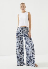 Witte geribbelde mouwloze top gecombineerd met brede marineblauwe broek met een wit bloemenpatroon. De broek heeft een trekkoord in de taille.