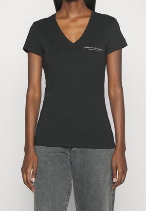 T-shirt noir à col en V en coton, avec des manches courtes et un logo doré discret sur le côté gauche de la poitrine. La coupe est ajustée.