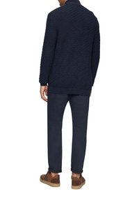 Marineblau gestrickter Pullover mit einem Rautenmuster, kombiniert mit dunklen Hosen und braunen Schuhen mit beigen Akzenten. Verfügt über gerippte Bündchen und Saum.