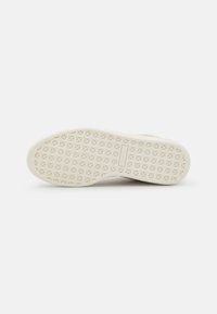 Semelle de chaussure plate blanche en caoutchouc avec motif d'étoiles croisées et petit logo rectangulaire au centre, vue par le dessous.