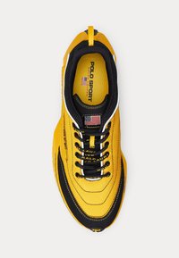 Gul och svart Polo Sport sneakers med snören, amerikansk flagga lappar och "Polo Sport Ralph Lauren" varumärke på innersulan och tungan.