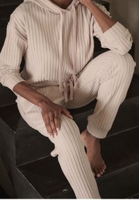 Jasno beżowy zestaw dresowy z prążkowanej tkaniny, składający się z bluzy z kapturem i sznurkiem oraz dopasowanych spodni, oba z miękkimi detalami teksturalnymi.