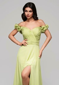 Abito verde chiaro con spalle scoperte, corpetto plissettato e dettagli floreali sulle maniche; presenta un alto spacco sulla coscia e un tessuto morbido e fluido.