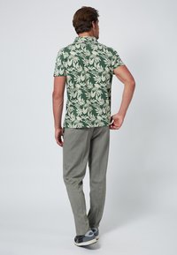 Camicia verde a maniche corte con motivo a foglie bianche, abbinata a pantaloni grigi chiari con texture e sneakers nere. Vista posteriore dell'outfit.