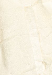 Tkanina z sztucznego futra w kolorze kremowym, o miękkiej fakturze; charakteryzuje się gładką, lekko błyszczącą powierzchnią z widocznym szwem oraz miękkim, gęstym włosiem.