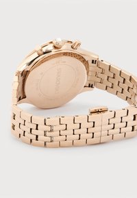 Ρολόι χειρός Swarovski από ανοξείδωτο ατσάλι σε ροζ χρυσό, με σύνδεσμο βραχιόλι, ορατή πίσω θήκη και κορώνα με κρυστάλλινη διακόσμηση.