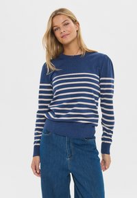 Modrá pruhovaná mikina s krémovými horizontálnymi pruhmi, okrúhlym výstrihom, rebrovanými lemami a manžetami. Kombinovaná s džínsami s vysokým pásom.