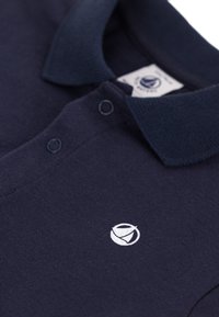 Polo shirt bleu marine avec un col, en tissu texturé et à patte de boutonnage à deux boutons. Logo blanc notable brodé sur le côté gauche.