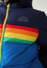 Kék puffertaka, vízszintes csíkokkal piros, narancssárga, sárga, zöld és türkiz színben. Cipzáras elülső rész, kapucni és szivárvány logó részlet.