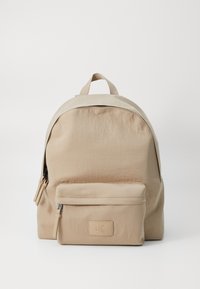 Zaino in nylon beige con forma arrotondata, dotato di una tasca frontale con zip, doppie maniglie superiori e una finitura testurizzata sottile.