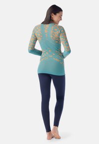 Top à manches longues en bleu sarcelle avec un motif floral orange et une texture lisse, associé à des leggings moulants bleu marine.