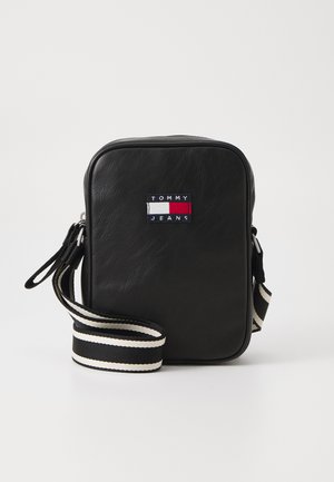 Black faux leather crossbody bag with a rectangular shape. Features a colorful "TOMMY JEANS" logo patch and a striped adjustable strap.