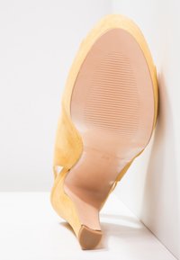 Žlutá semišová lodička na vysokém podpatku s špičatou špičkou, hladkou koženou podrážkou a mírně zakřiveným zadním dílem. Velikost 38 je uvedena uvnitř.