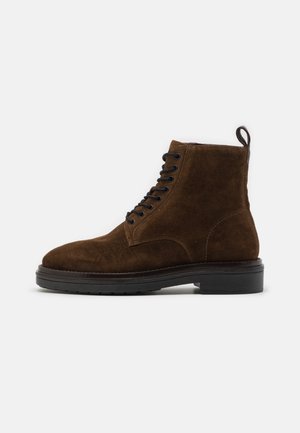 Brown suede ankle boots with a rounded toe, black laces, a pull tab at the back, and a thick black rubber sole.