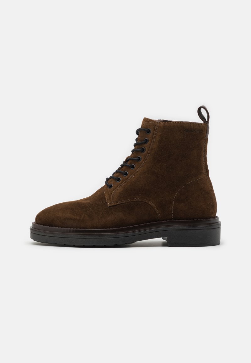 Brown suede ankle boots with a rounded toe, black laces, a pull tab at the back, and a thick black rubber sole.