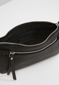 Musta nahkainen clutch-laukku hopeisella vetoketjulla, jossa pääosiolla ja sisäisellä vetoketjutaskulla, sileä pinta ja minimalistinen muotoilu.