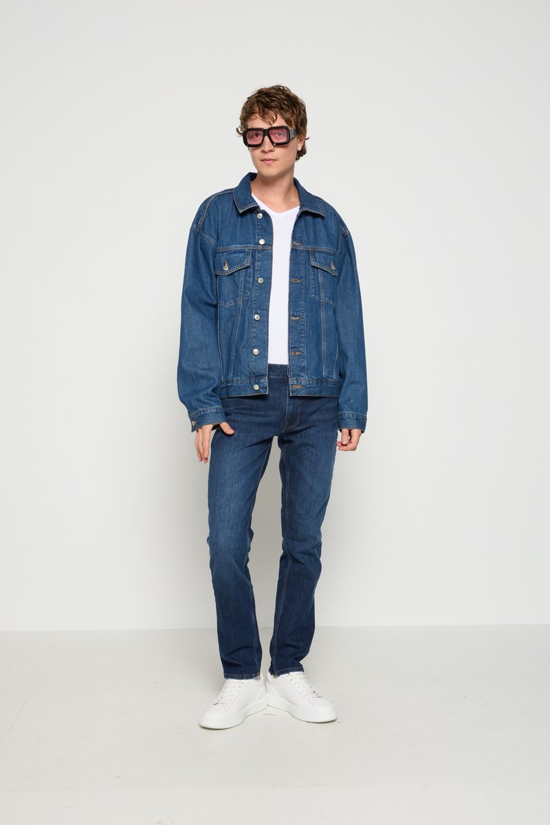 Jeansowa kurtka z frontowymi kieszeniami, zestawiona z białą koszulką i ciemnoniebieskimi dżinsami. Białe trampki i oversize'owe różowe okulary przeciwsłoneczne dopełniają całość.