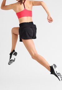 Urheiluasu, johon kuuluu vaaleanpunainen urheiluliivit, mustat shortsit teksturoidulla pinnalla ja mustavalkoiset juoksukengät kuvioidulla pohjalla.