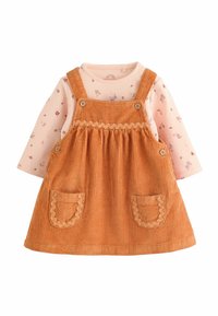 Robe en velours côtelé orange avec des poches à bords festonnés, associée à une chemise à manches longues rose ornée de petits motifs floraux.