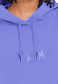 Paarse hoodie met een kangoeroe-pocket, koordjes met gouden tips en geborduurde tekst op de borst. Soepele katoenstof.