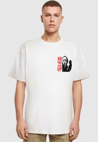 Hvid bomulds t-shirt med et grafikdesign, der viser en sort-hvid maske og rød tekst, der står "NEJ, DU LÆGGER PÅ," kortærmet.