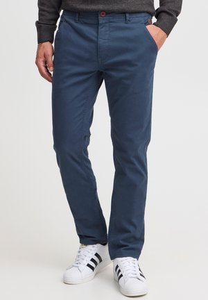 Herrnavyblå chinos tillverkade av bomullsblandning, med rak skärning, två sidofickor och knappstängning. Bärs med vita sneakers.