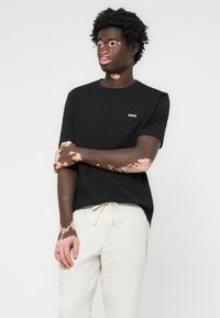 Black cotton crew-neck t-shirt with a small white "BOSS" logo on the chest. Worn with light beige drawstring pants.