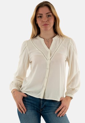 Blusa blanca de botones con un tejido texturizado, escote redondo y mangas abullonadas. Presenta un bordado ornamentado a lo largo de las costuras del cuerpo.