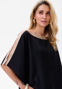 Zwarte oversized top met beige zijden accenten bij de halslijn en mouwen; gladde textuur, brede mouwen en een relaxte pasvorm.