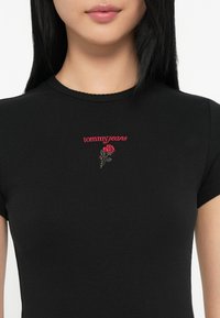 Crna rebrasta majica kratkih rukava s okruglim izrezom, s crvenim "tommyjeans" natpisom i izvezenim detaljem ruže na prsima.