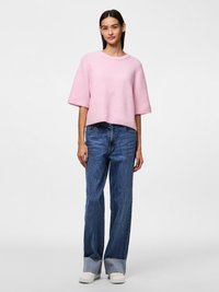 Camisola curta rosa claro de malha com mangas curtas, combinada com jeans azul escuro de perna larga com bainha desfiada e sapatilhas brancas.