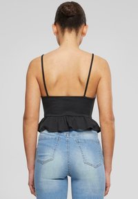 Black ribbed peplum top with thin straps, featuring a flared hem. Paired with light blue, fitted denim jeans showing back pockets.