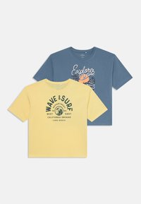 Två t-shirts med kort ärm: en i gult med grön grafisk text och v�ågmönster, den andra i blått med en färgglad "Utforska"-tryck.