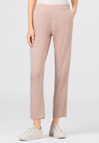 Light pink, slim-fit pants made of soft fabric with a smooth texture, featuring a waistband and paired with white sneakers.