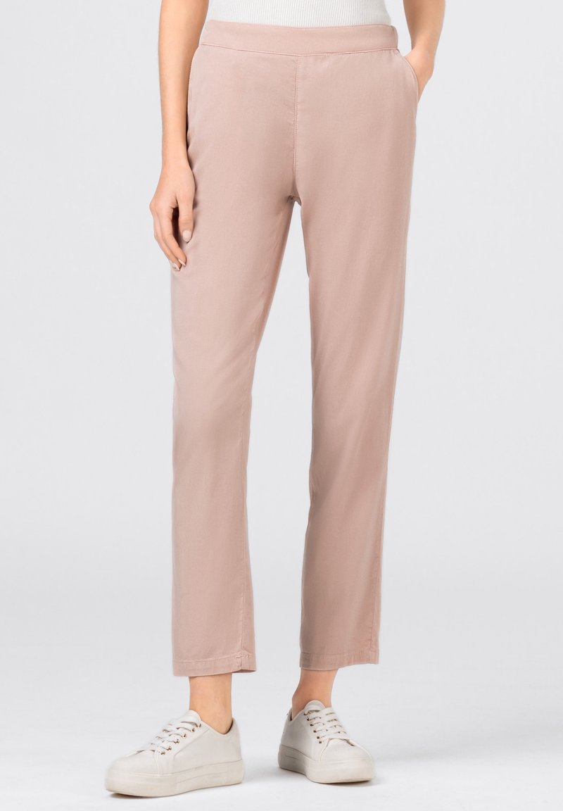 Light pink, slim-fit pants made of soft fabric with a smooth texture, featuring a waistband and paired with white sneakers.