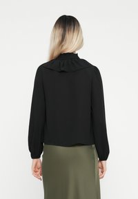 Black blouse with a ruffled collar, long sleeves, and a loose fit, paired with a smooth, olive-green skirt.