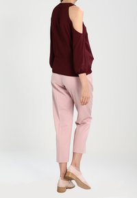 Bordeaux-farvet kold-shoulder top med ballonærmer, parret med lyserøde, tapered bukser og beige sko med træhæle.