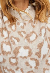 Sweter dzianinowy z beżową podstawą i jasnobrązowymi plamkami w leoparda, teksturowany materiał oraz okrągły dekolt z falbaną białej podszewki.