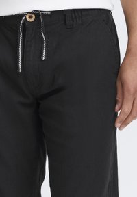 Zwarte broek van lichtgewicht stof, met een trekkoord met een witte accent. Zichtbare knoopsluiting, schuine zijzakken.