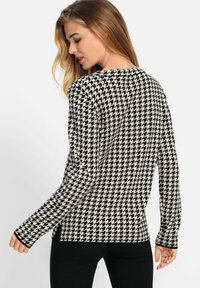 Schwarzer und cremefarbener Hahnentrittmuster langärmeliger Pullover mit rundem Ausschnitt und eng anliegenden Ärmeln, gefertigt aus einem weichen Textil.