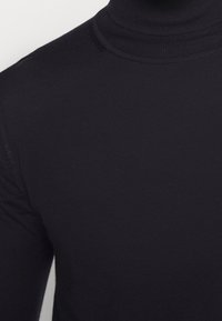 Schwarzer Rollkragenpullover mit gerippter Textur, figurbetontem Design und hohem Kragen. Das Material wirkt weich und dehnbar.