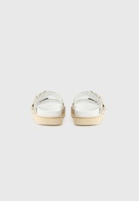 Sandali in plastica trasparente con suola piatta beige e dettagli decorativi a forma di fiocco. Le cinghie sono trasparenti con ulteriori dettagli.