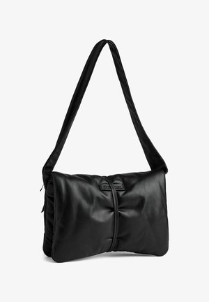 Borsa a mano nera in morbida pelle con una forma rettangolare strutturata; presenta una spessa tracolla piatta e un accentuato fermo centrale con una patch del logo.