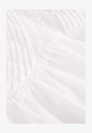 White fabric featuring pleats and gathered texture, showing a light, airy quality with soft, smooth surface.