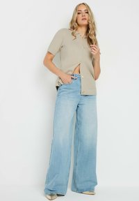 Cardigan beige à manches courtes avec fermeture à boutons, associé à un jean large bleu clair. Tissu lisse avec une coupe décontractée.