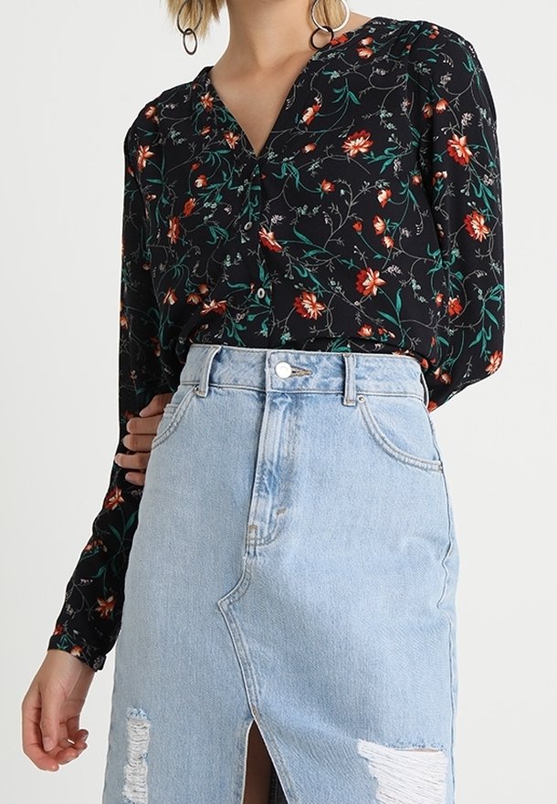Blouse noire à fleurs avec manches longues et encolure en V, associée à une jupe en denim bleu clair avec une fente avant et des détails usés.